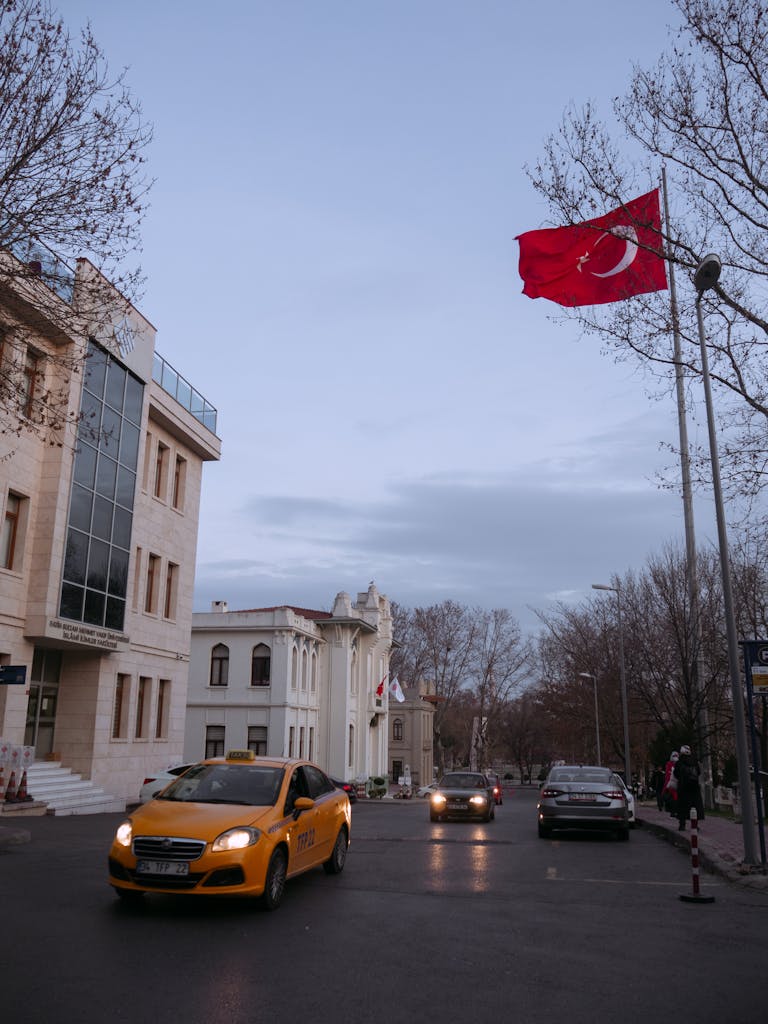 Mersin sokak sahnesi; Türk bayrağı ve akşam saatlerinde trafikli bir ortamla kültürel ve kentsel yaşamı yansıtıyor.